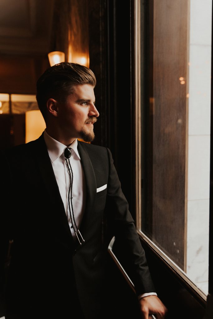 Groom in bolo tie looking out window at Le Meridien tampa