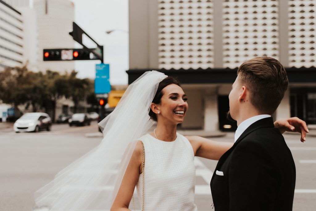 Bride in veil smiling at groom on downtown street