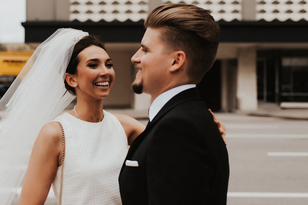 Bride in veil smiling at groom on downtown street