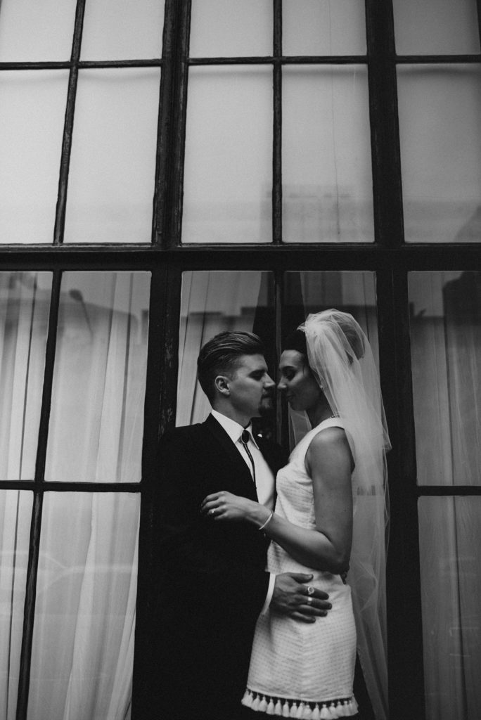 Bride and groom facing each other in front of black window