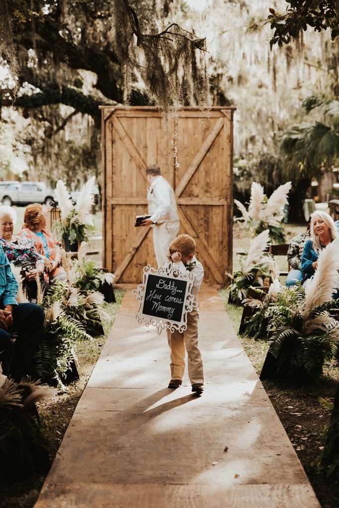 Ring bearer walking down the aisle during oak trees for okeechobee florida wedding ceremony