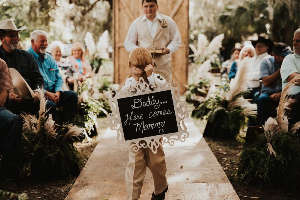 Ring bearer walking down the aisle during oak trees for okeechobee florida wedding ceremony