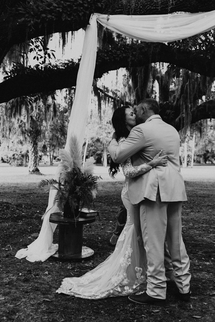 Bride and groom first kiss under oak trees in outdoor ceremony in Okeechobee Florida