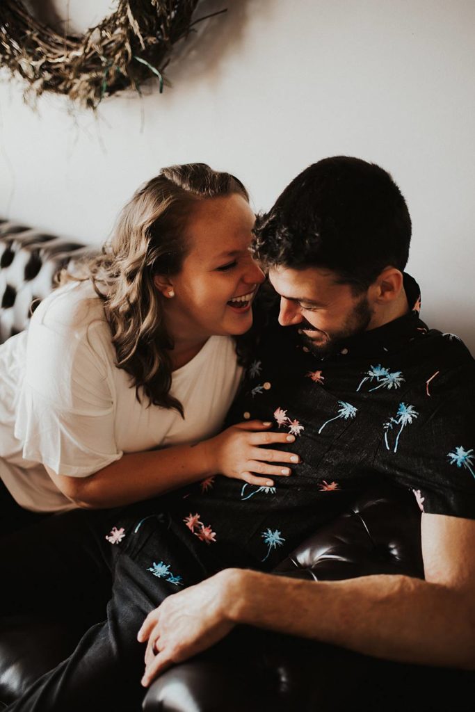 Couple sitting on couch laughing during engagement session at brewery