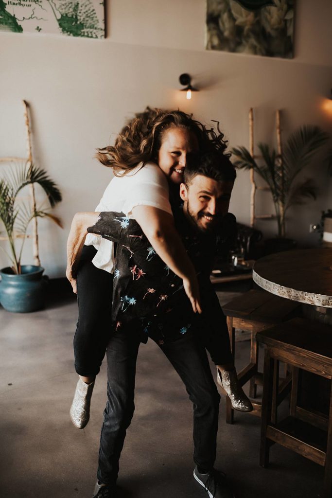 Couple giving piggy back ride during engagement session at brewery