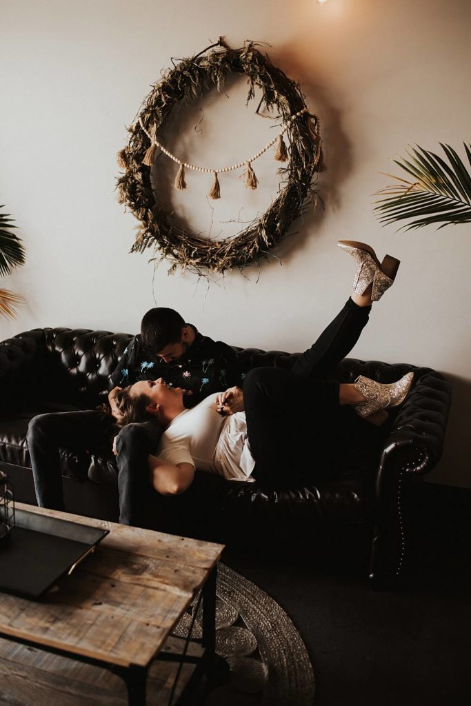 Couple sitting on couch laughing during engagement session at brewery