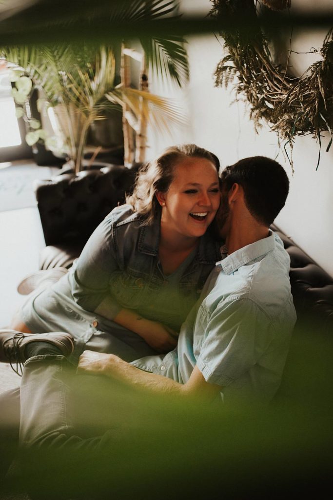 Couple sitting on couch laughing during engagement session at brewery