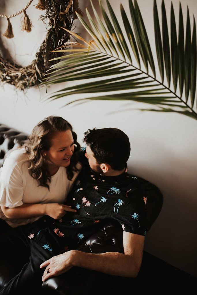 Couple sitting on couch laughing during engagement session at brewery