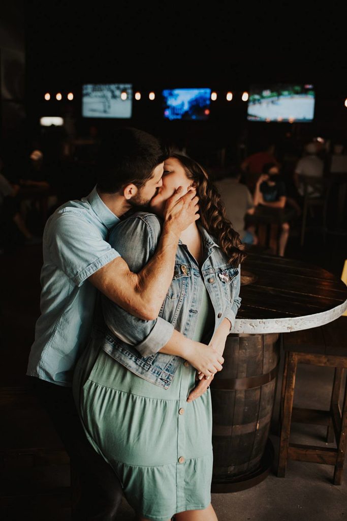 Couple kissing during engagement session inside brewery