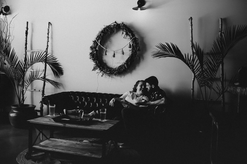 Couple sitting on couch laughing during engagement session at brewery