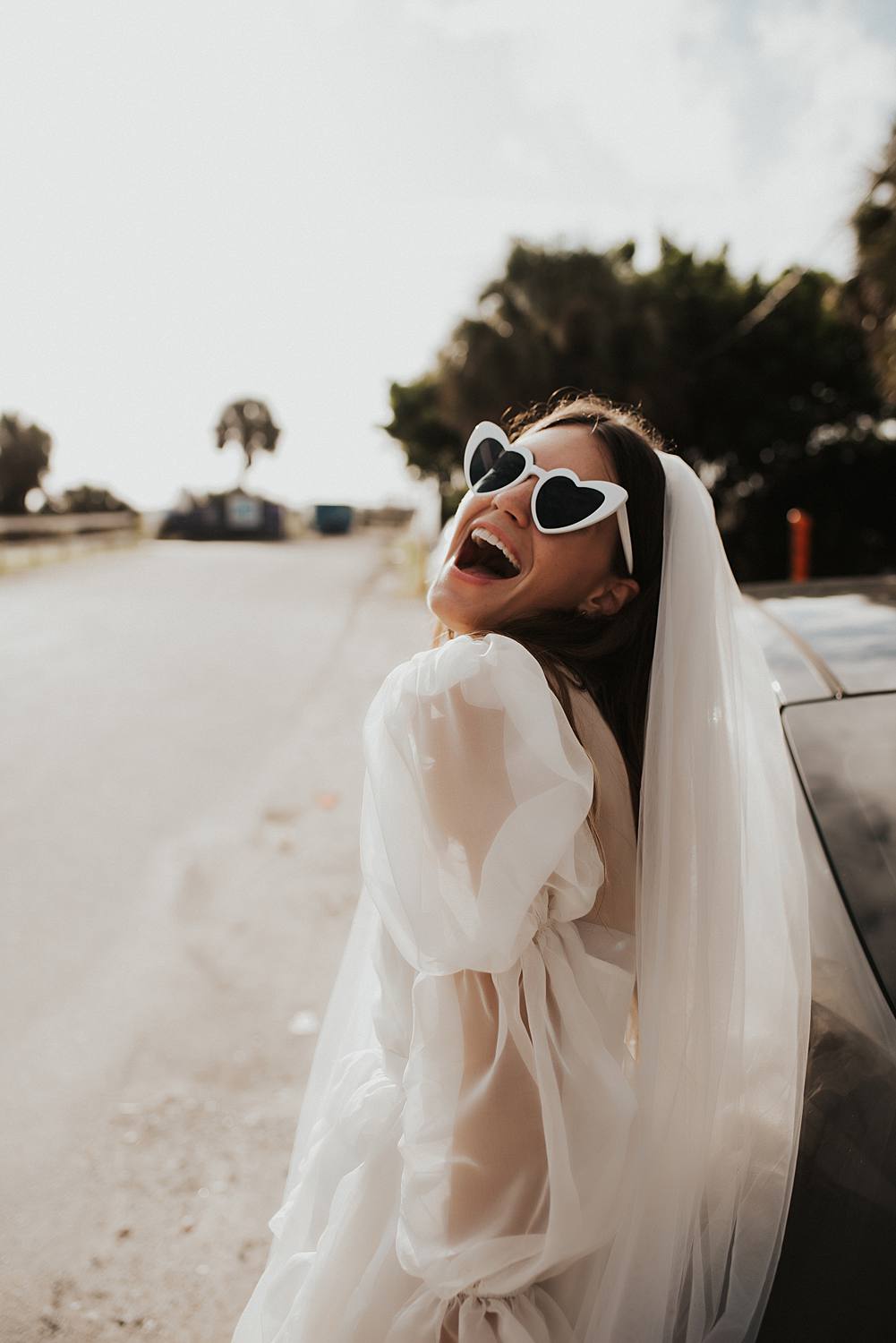 Bride in sunglasses with veil leaning on car