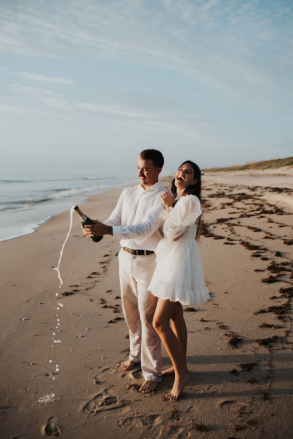 Bride and groom popping champagne on beach