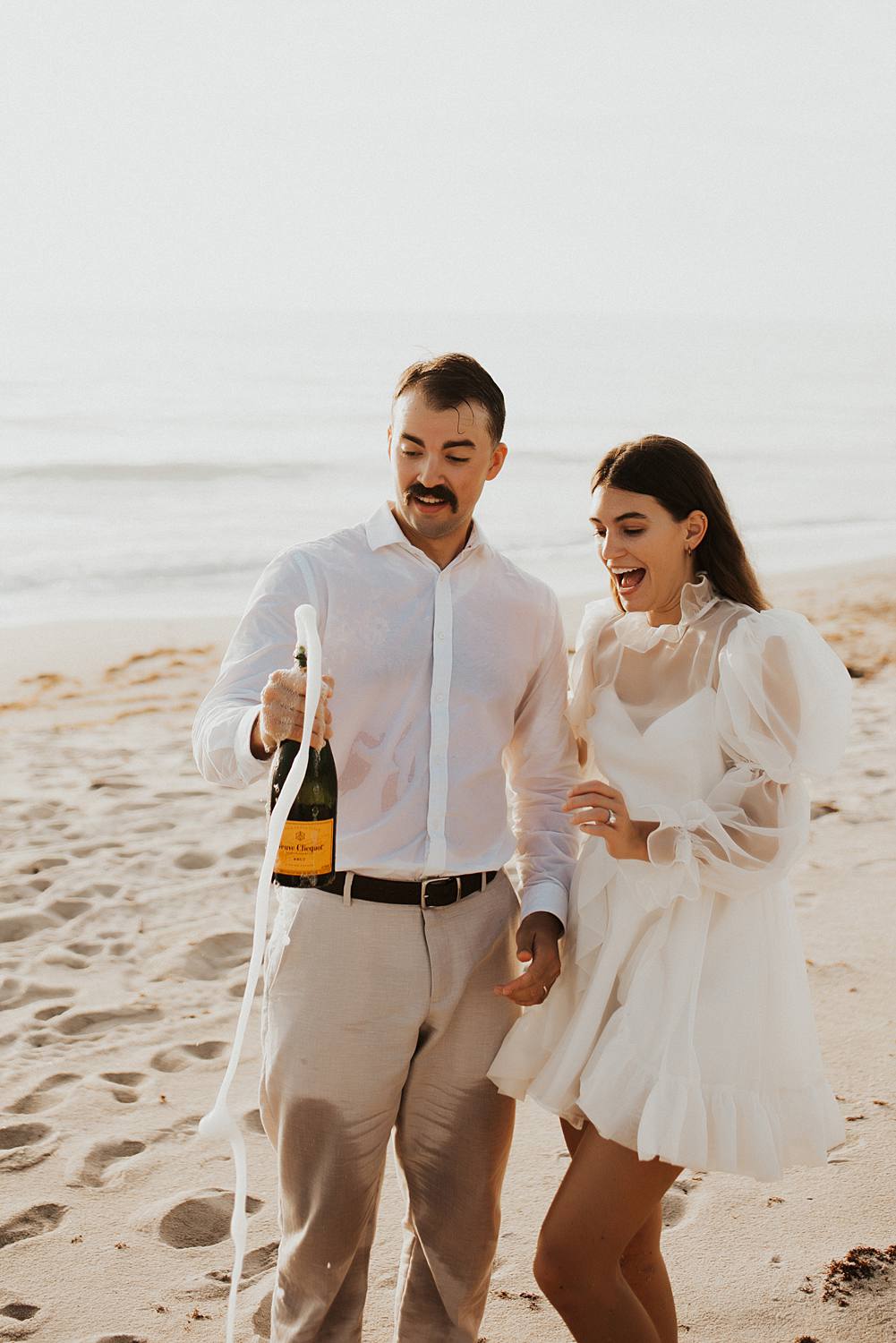 Bride and groom popping champagne on the beach