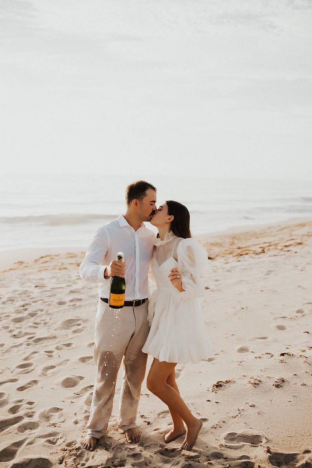 Bride and groom popping champagne on the beach