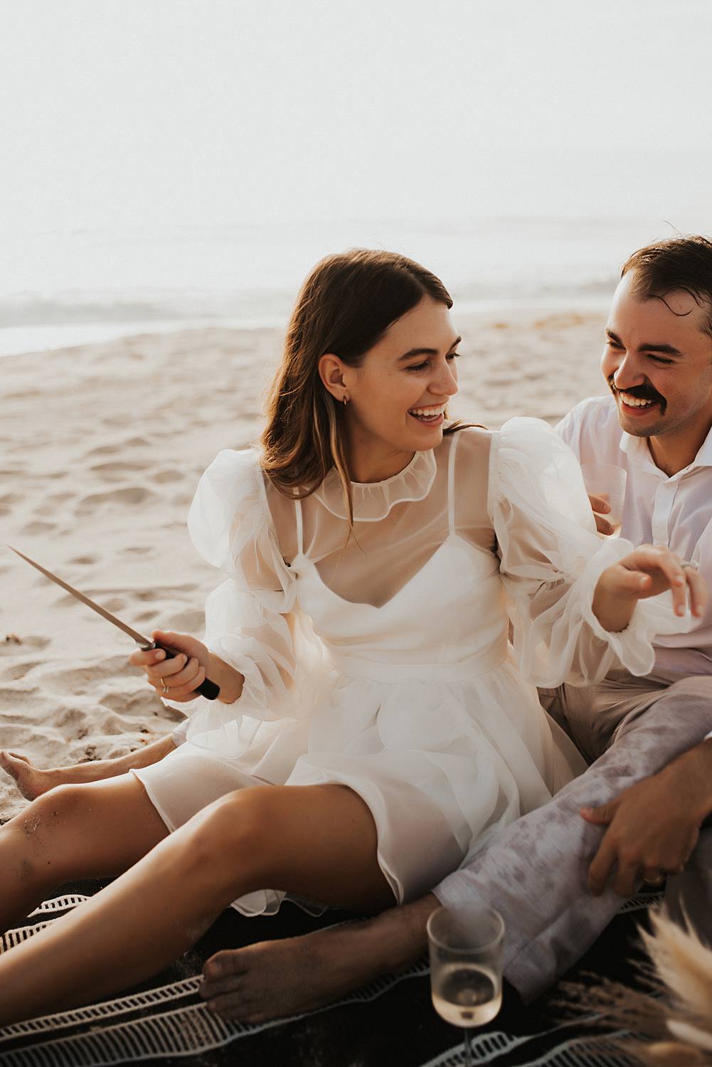 Bride cutting cake during elopement picnic on beach