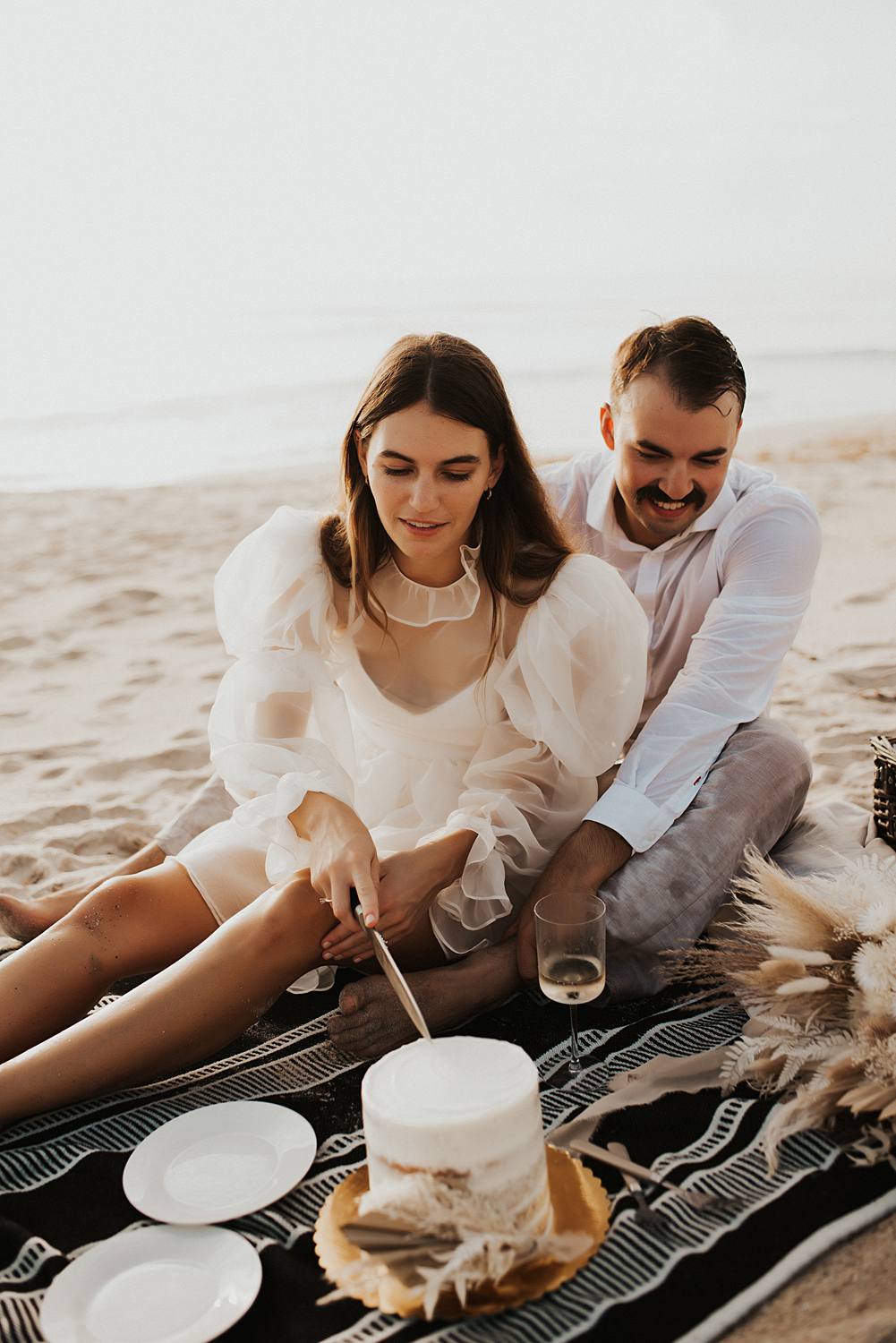 Bride cutting cake during elopement picnic on beach