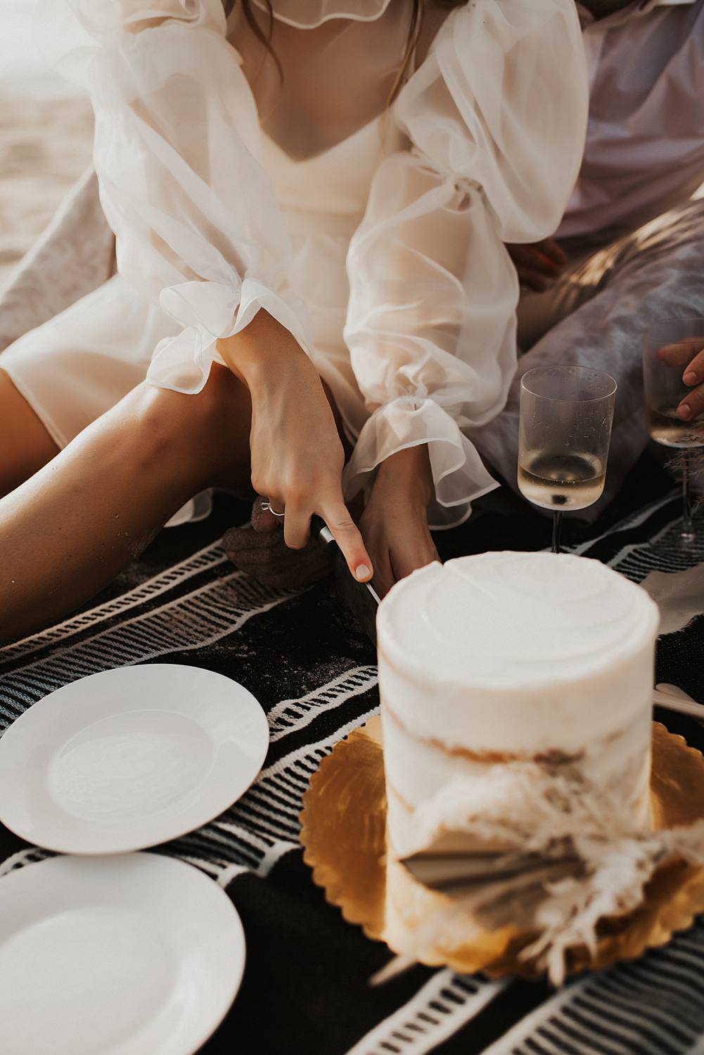 Bride cutting cake during elopement picnic on beach