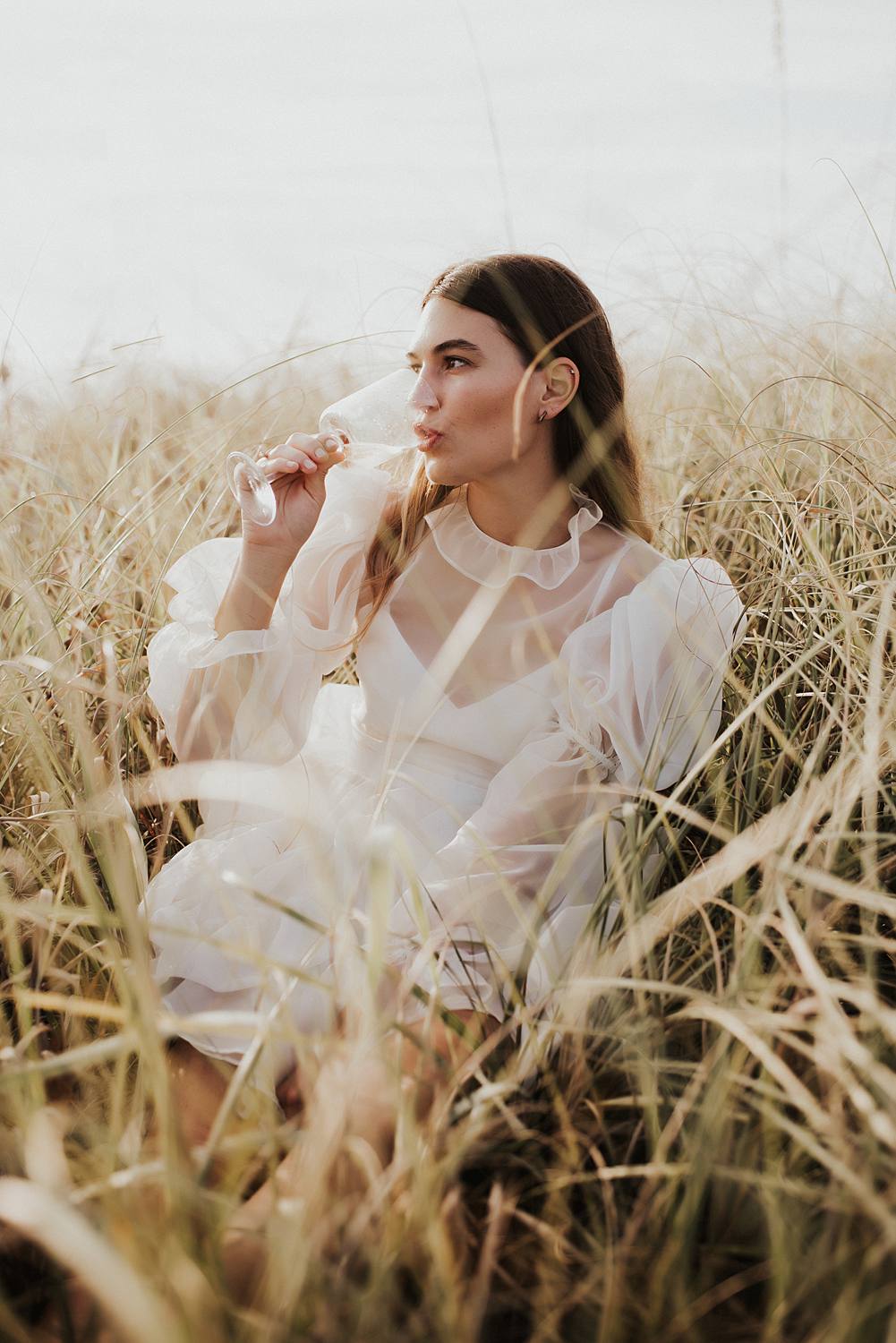 Bride drinking champagne in tall beach grass