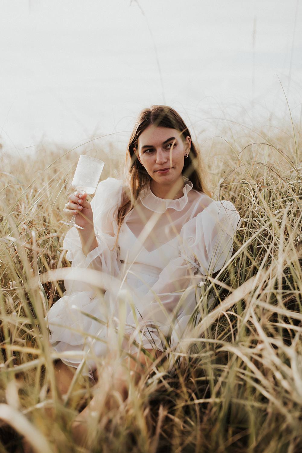 Bride drinking champagne in tall beach grass