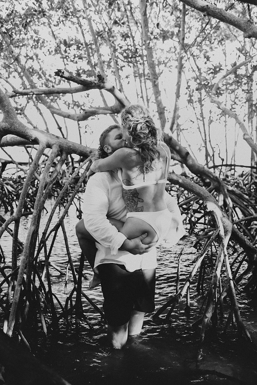 Groom lifting bride in white bikini in mangrove trees