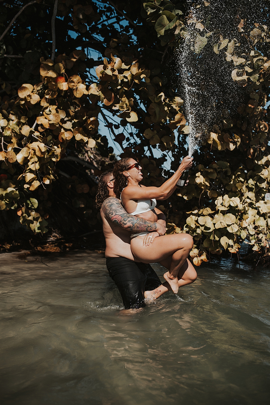 Bride popping champagne in water in front of mangroves