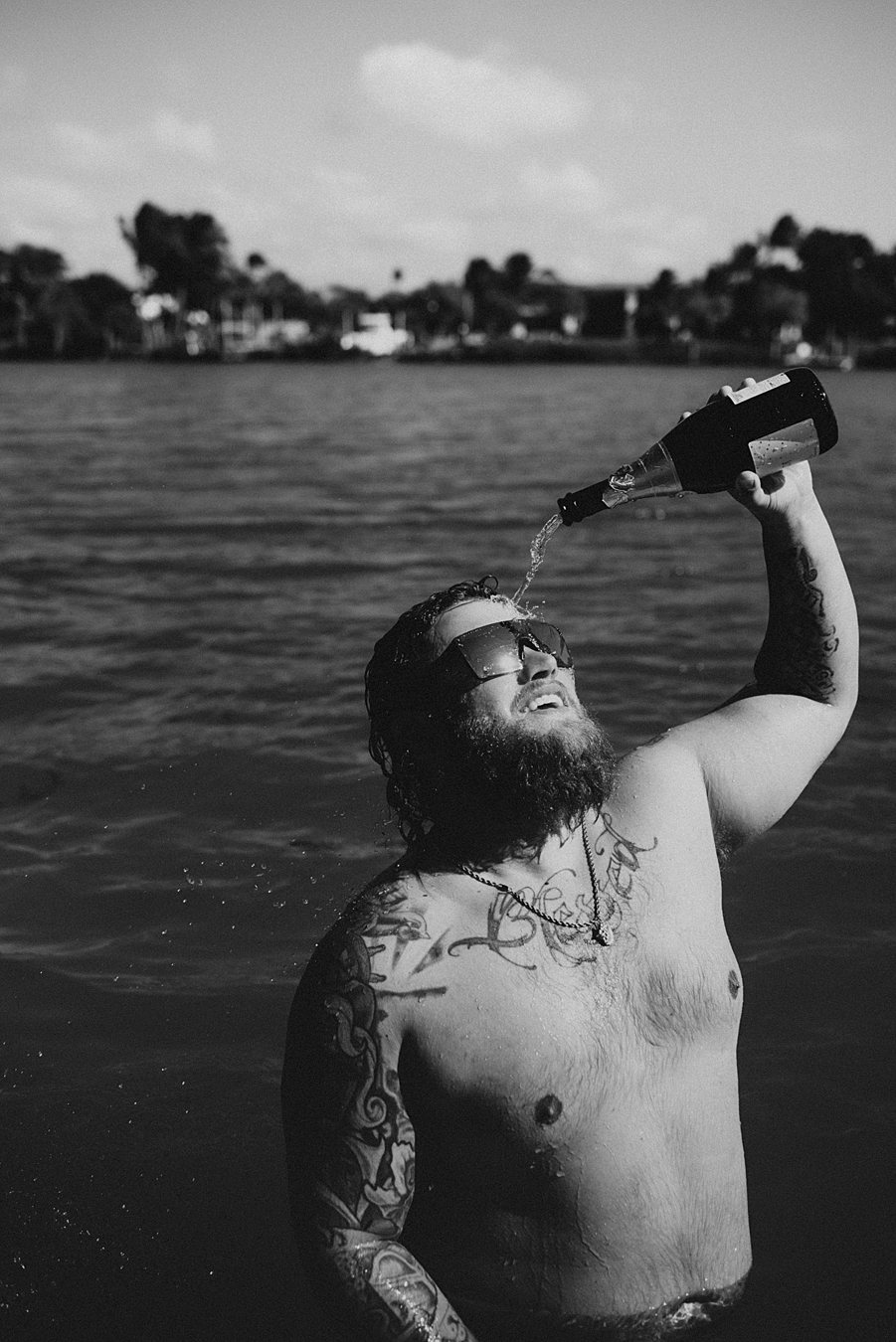 Groom pouring champagne over head in water