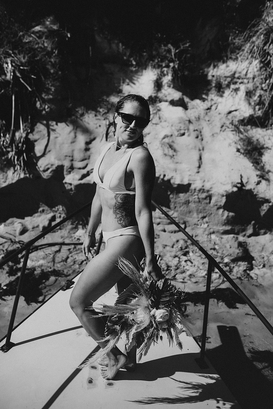 Bride in bikini with dried floral bouquet on front of boat