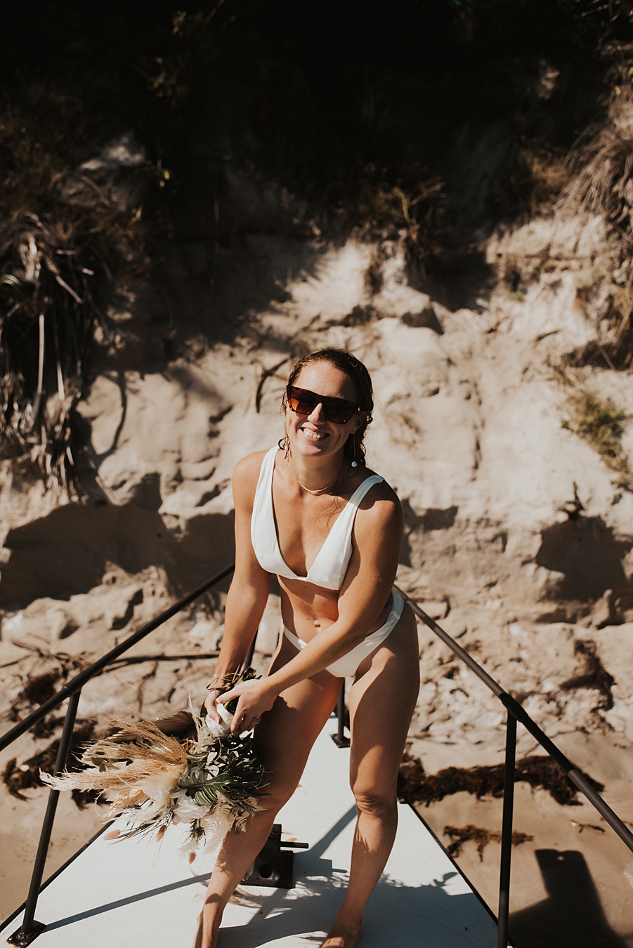 Bride in bikini with dried floral bouquet on front of boat