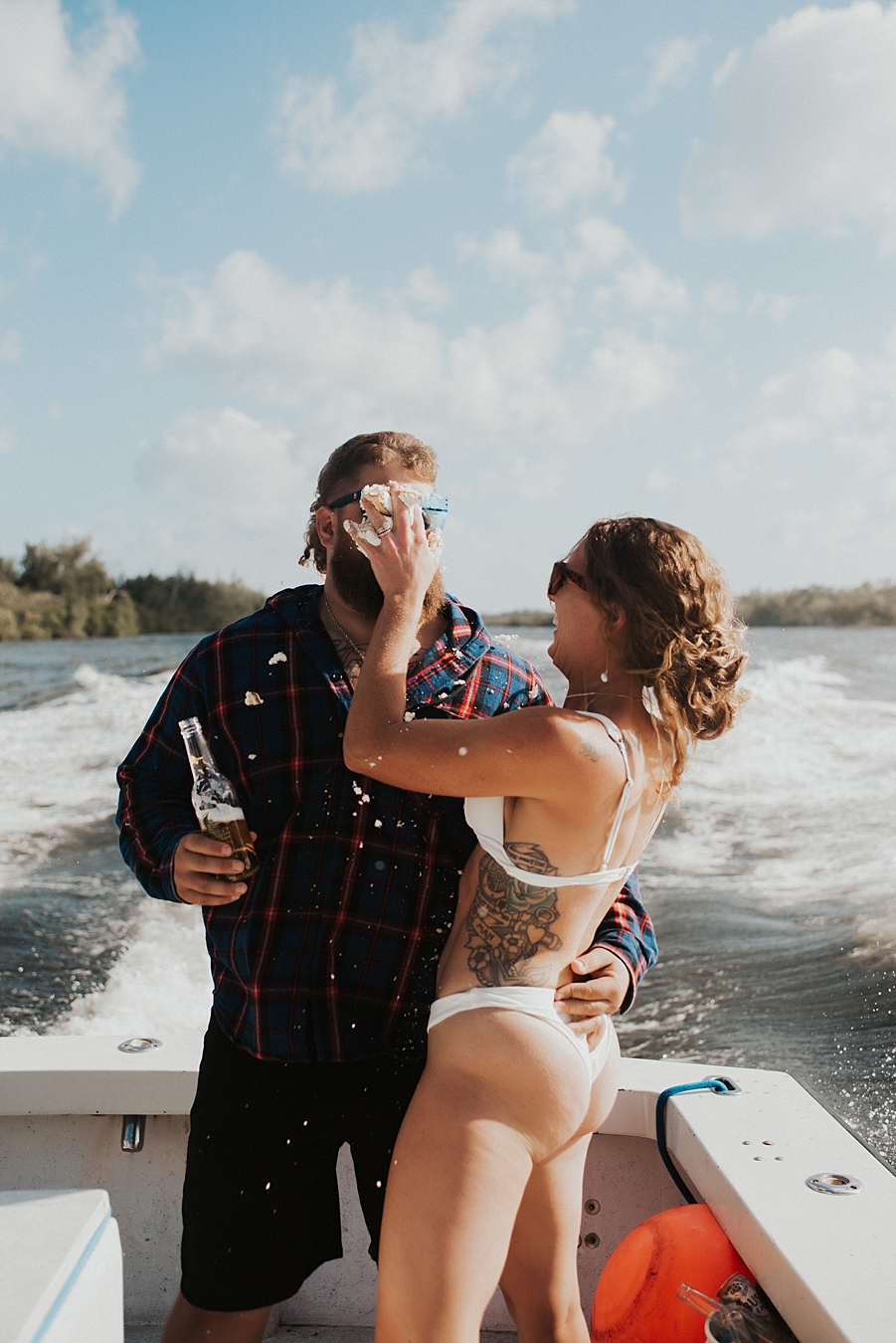 Bride in bikini smashing cake into grooms face on boat