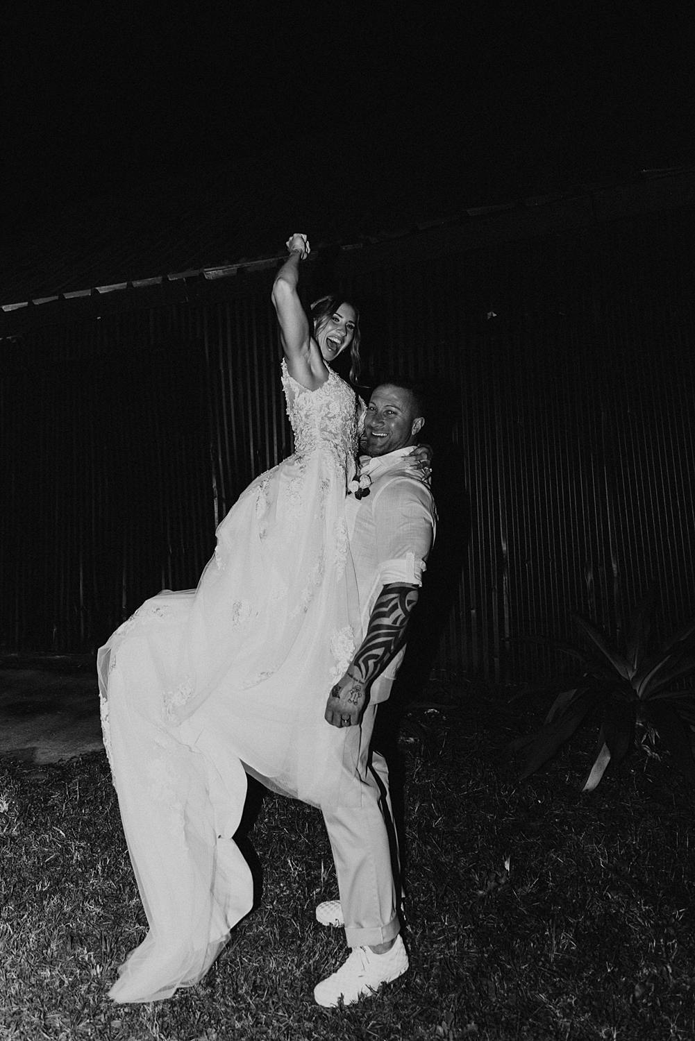 Groom picking up bride and bride throwing fist into air