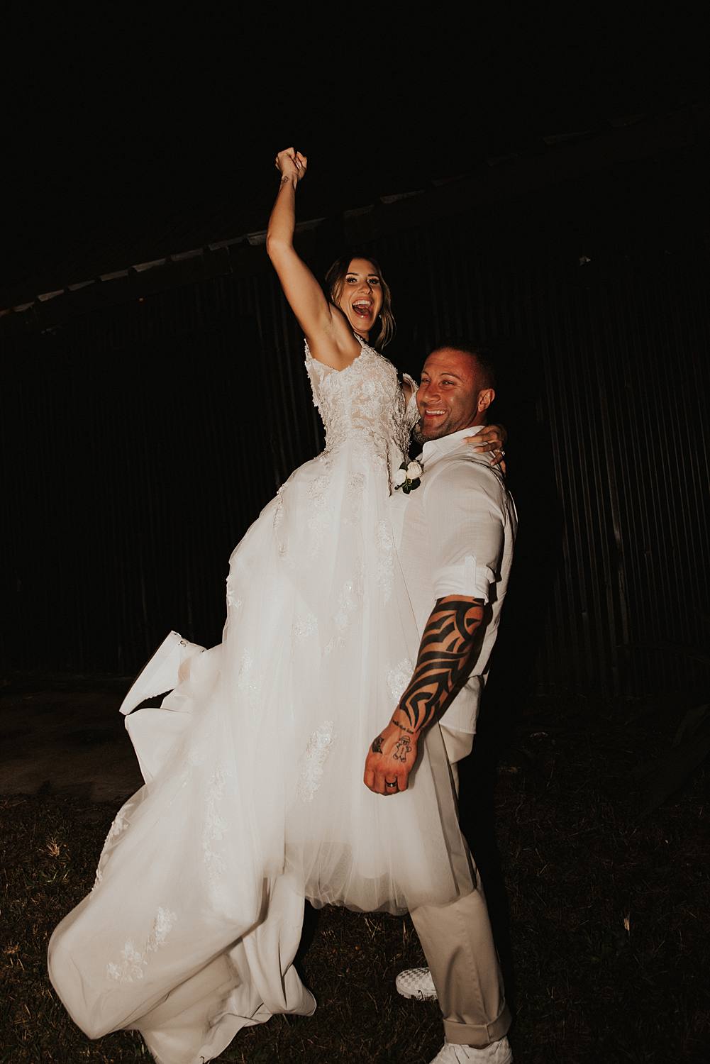 Groom picking up bride and bride throwing fist into air