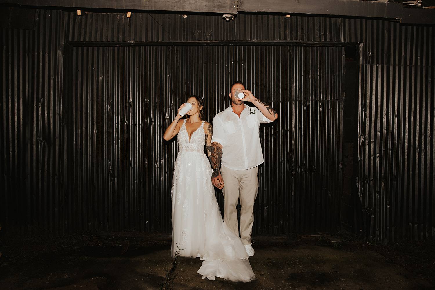 Bride and groom drinking champagne out of cups in front of black wall