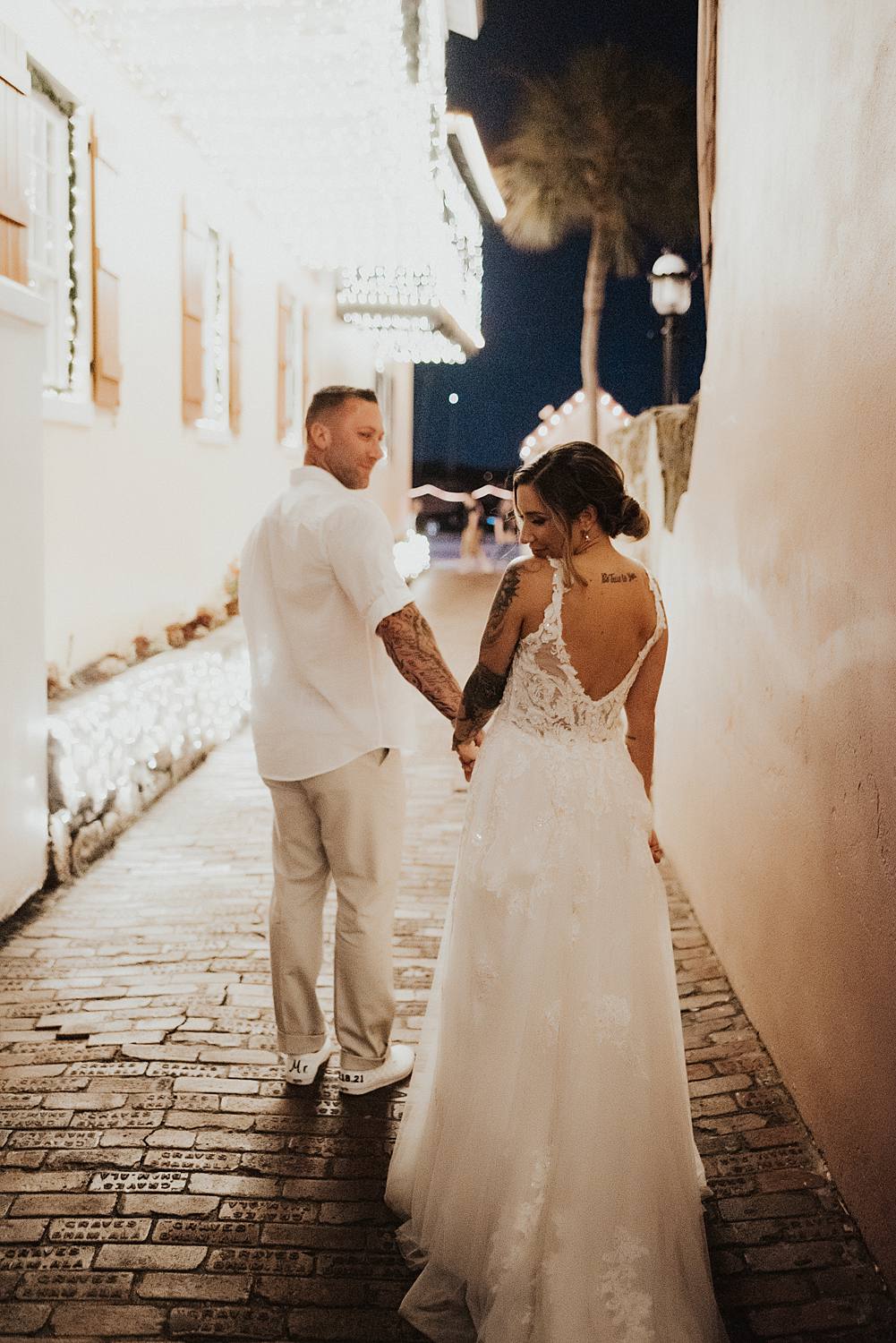 Bride looking down as groom leads her down alleyway
