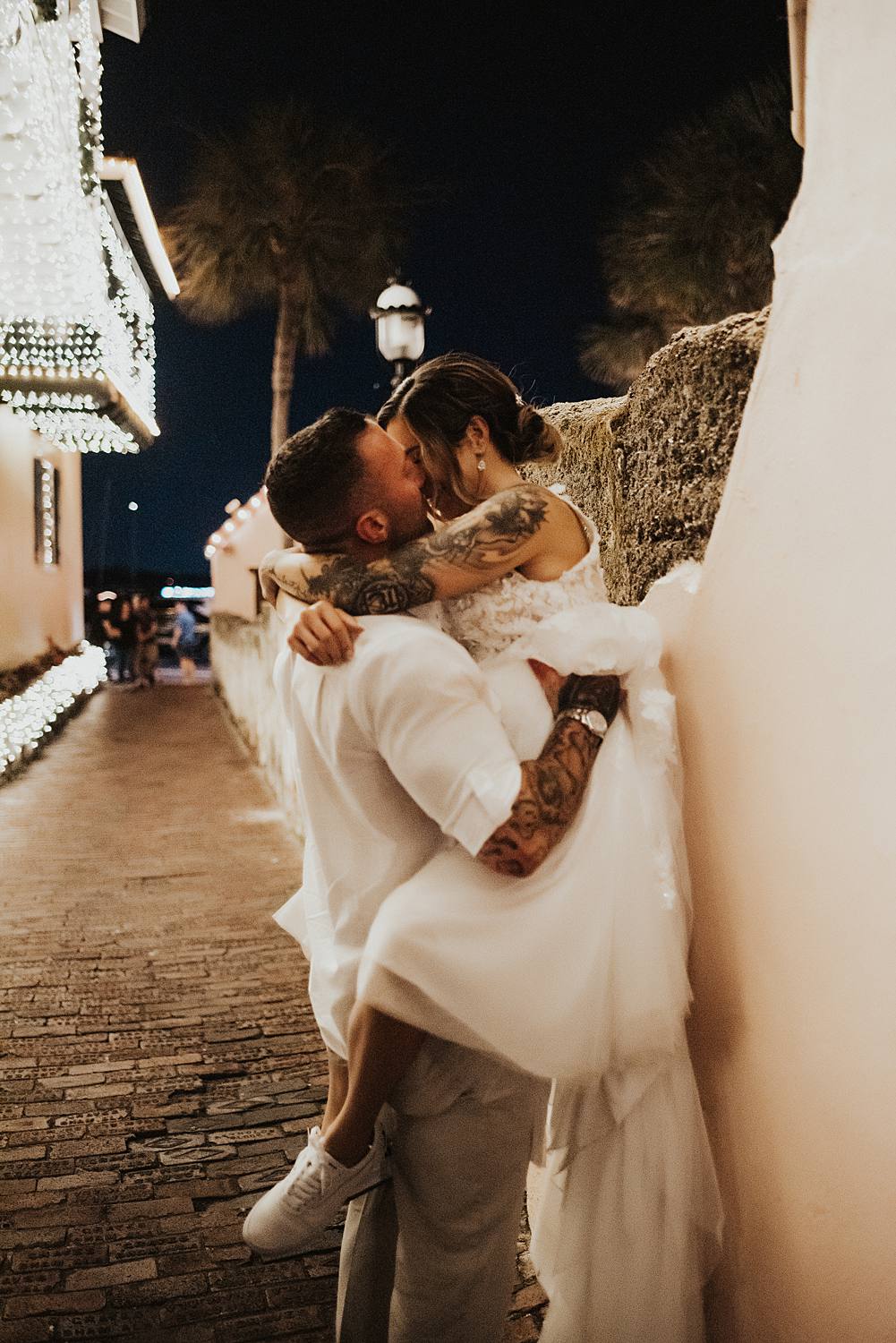 Groom picking up bride and pushing her against a wall in an alleyway