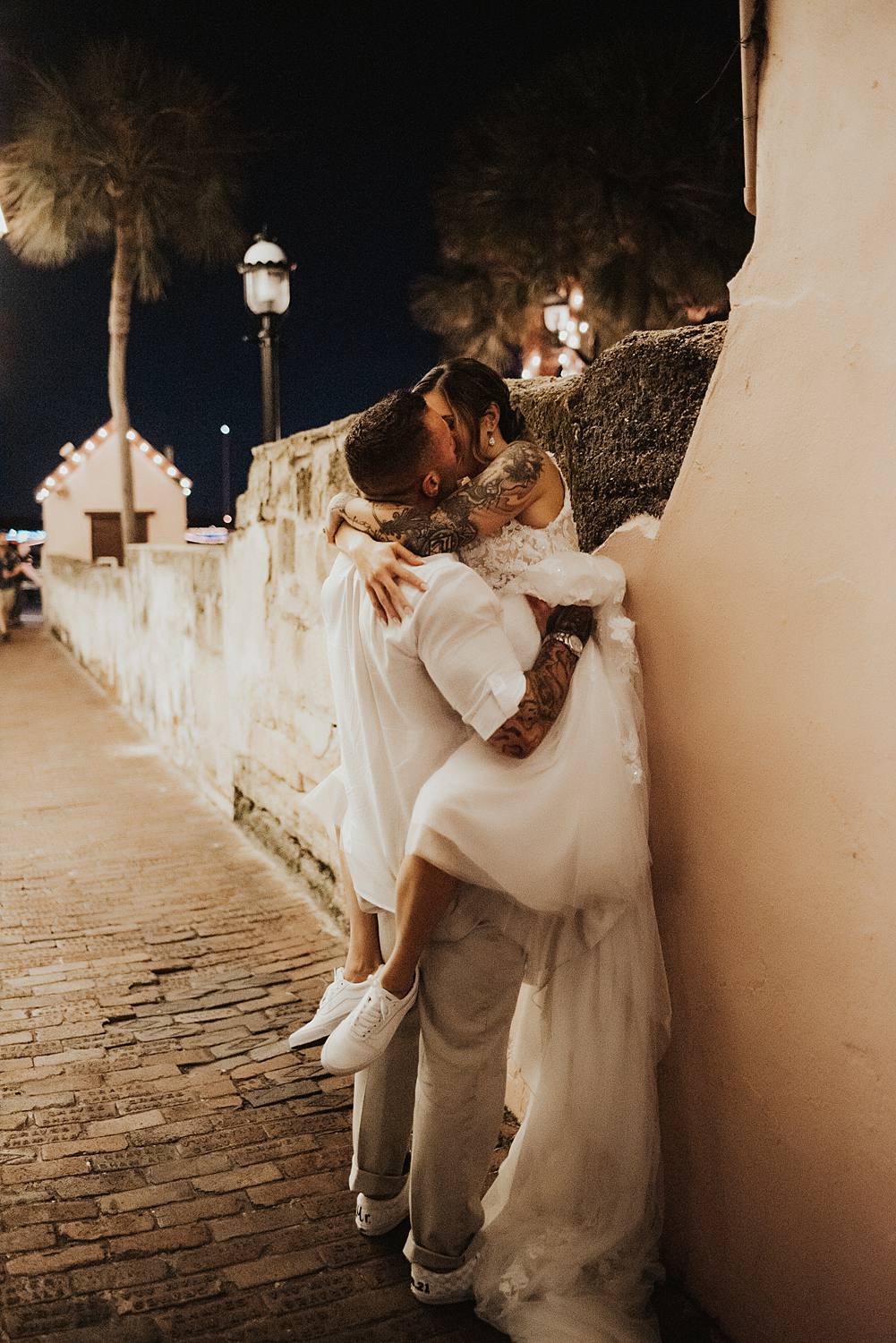 Groom picking up bride and pushing her against a wall in an alleyway