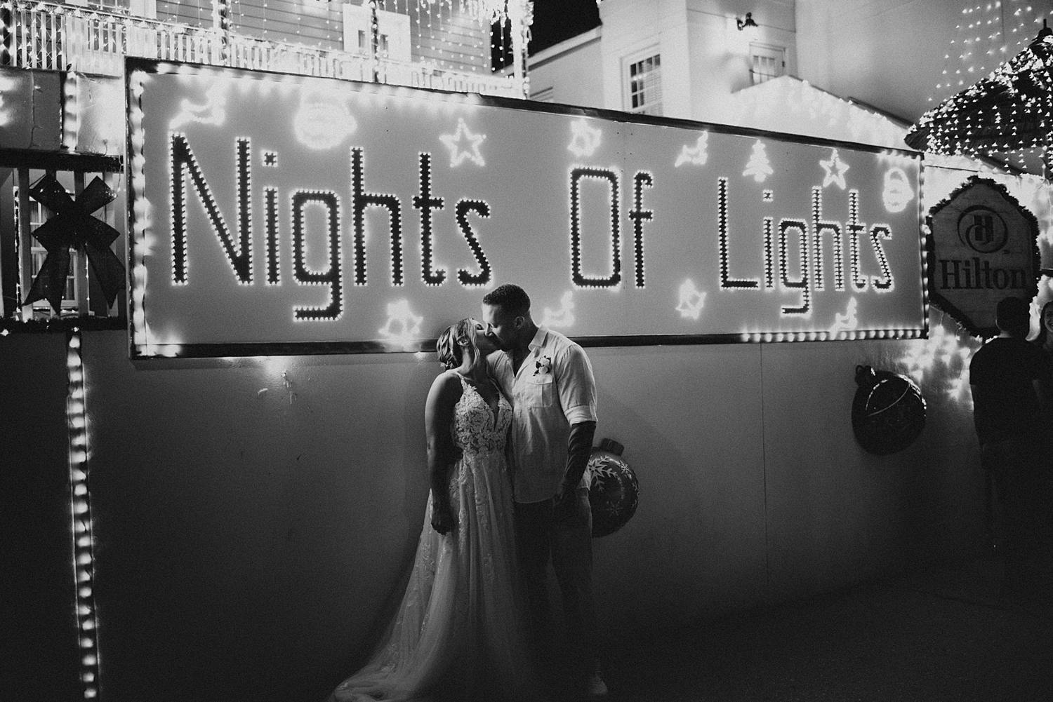 Bride and groom kissing in front of night of lights sign