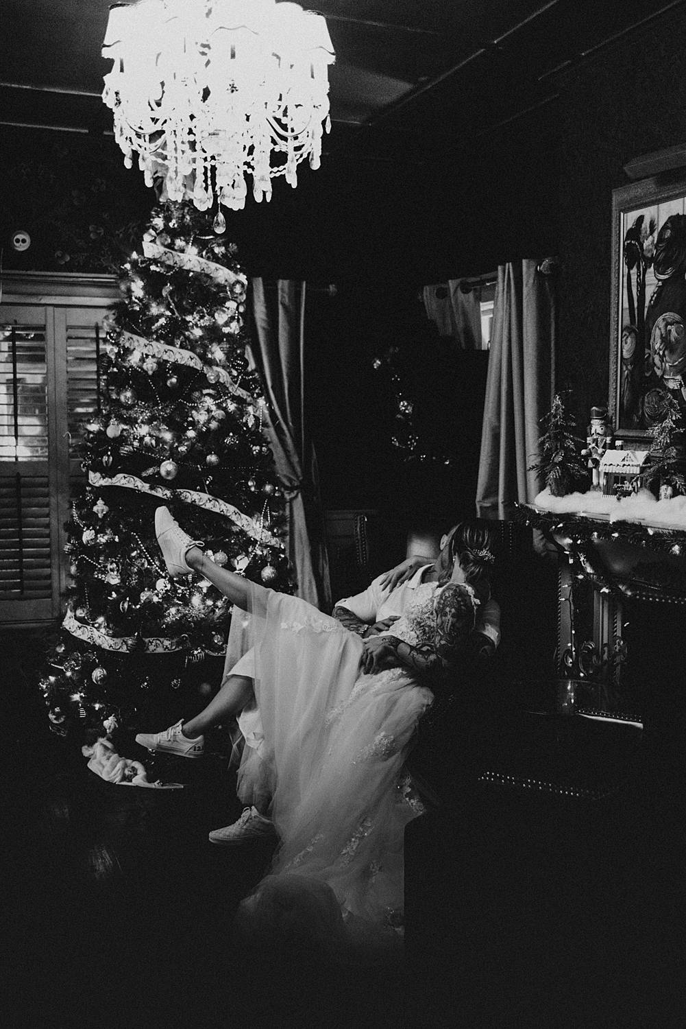 Bride sitting on grooms lap in front of Christmas tree at the Tini Martini