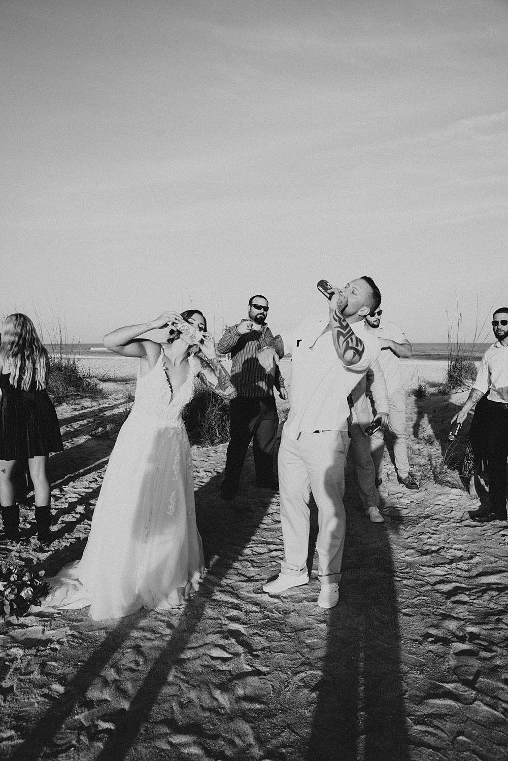 Bride and groom shotgunning beer after beach ceremony