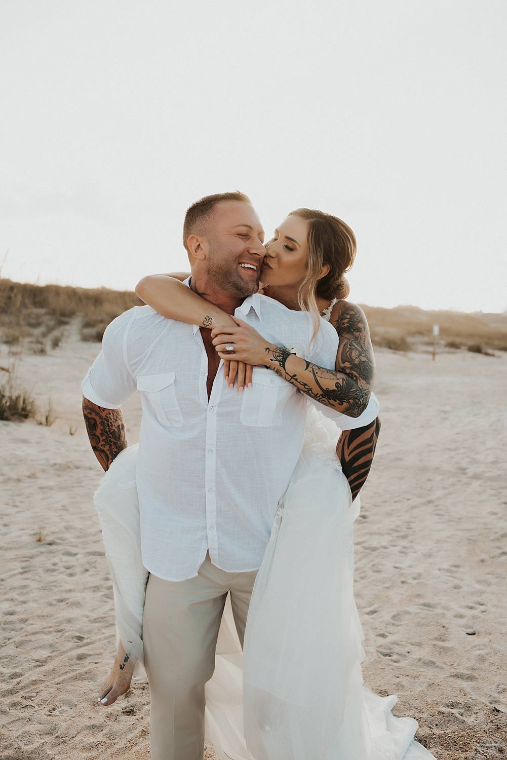 Bride getting piggyback ride from groom on beach