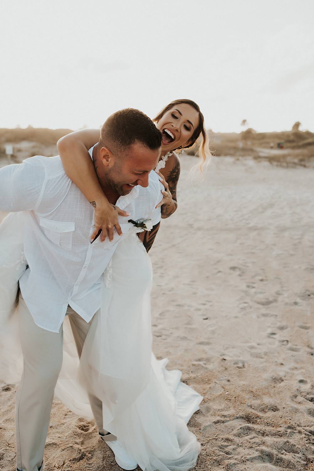 Bride getting piggyback ride from groom on beach