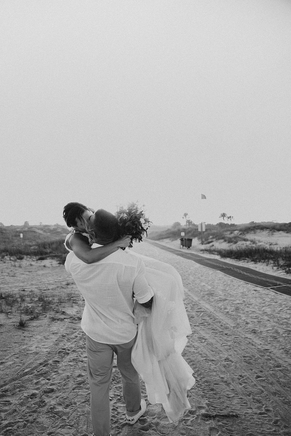 Groom carrying bride away on Saint Anastasia beach