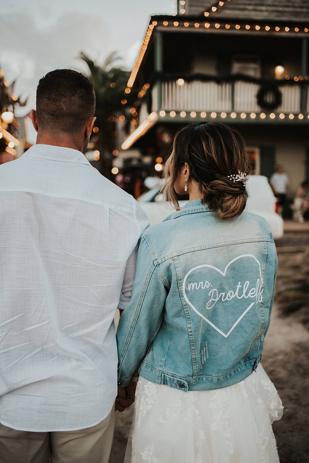 Bride in custom jean jacket holding groom's hand on Saint George street