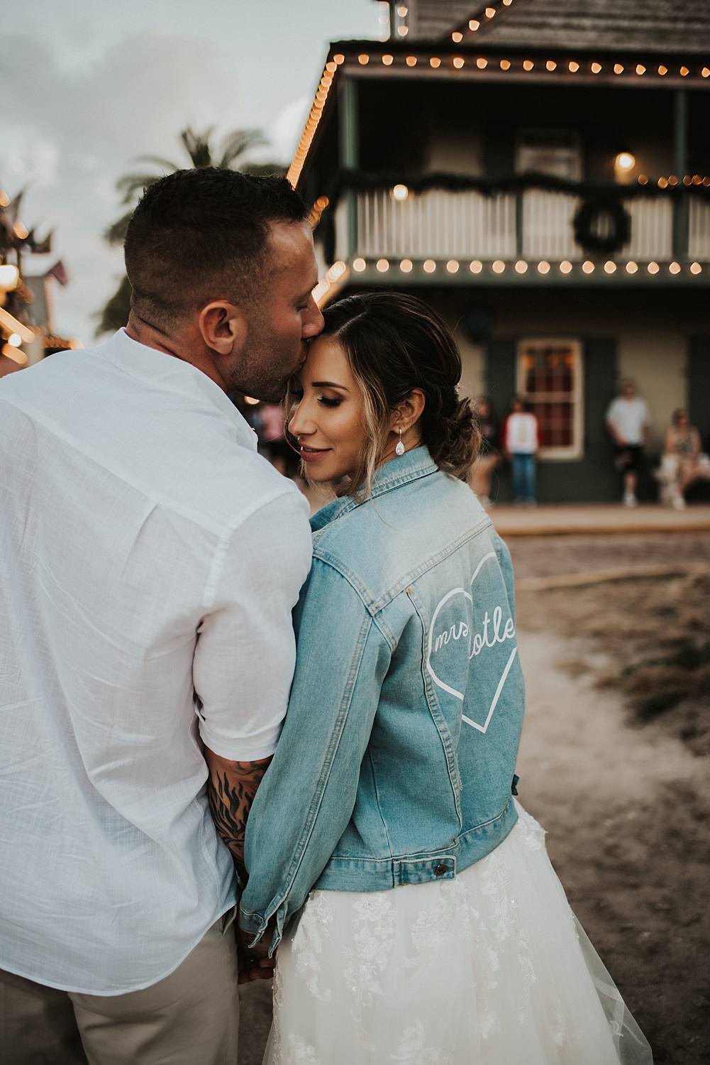 Groom kissing brides forehead in custom jean jacket