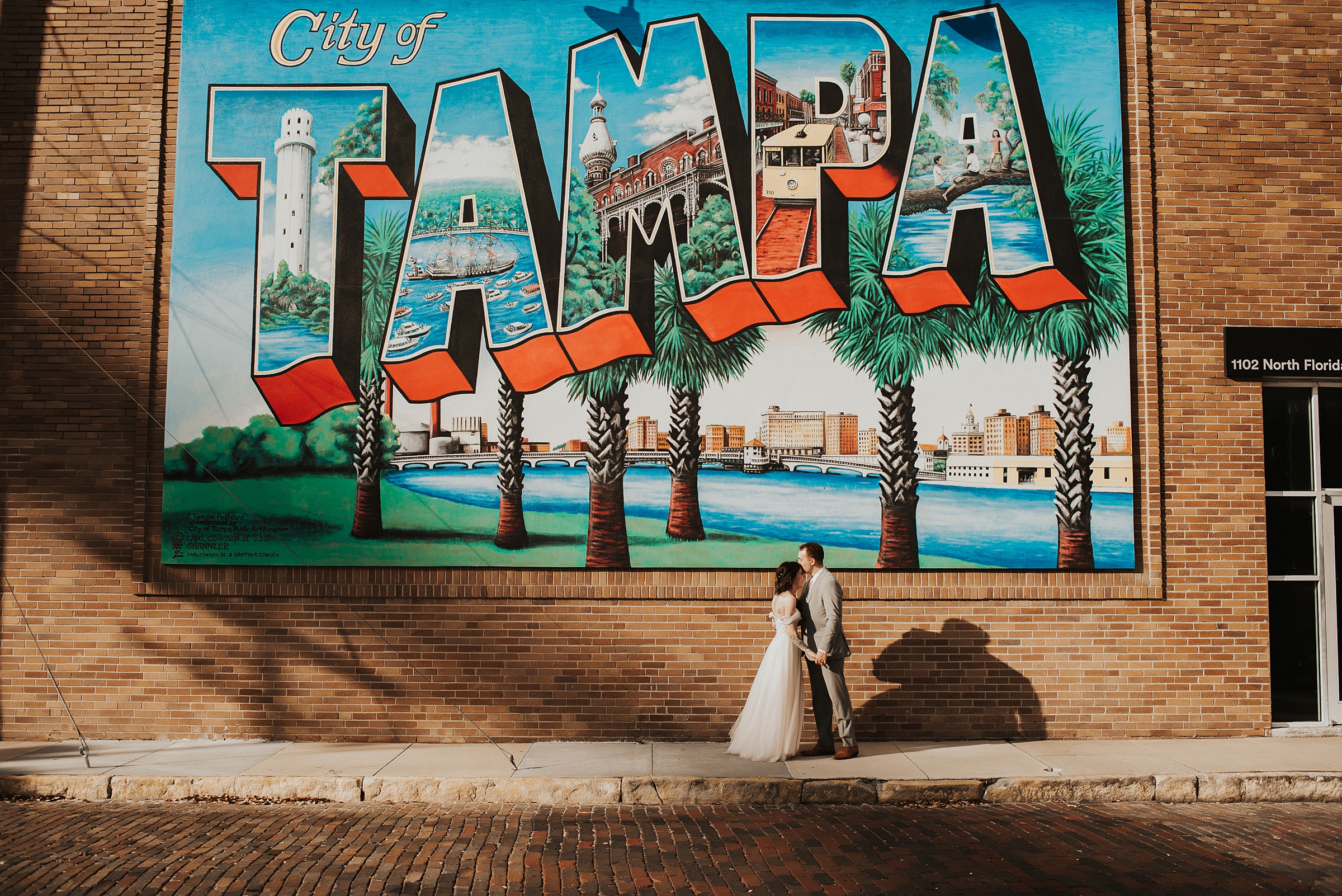 Groom kisses the top of brides head in front of large Tampa mural after their downtown Tampa elopement