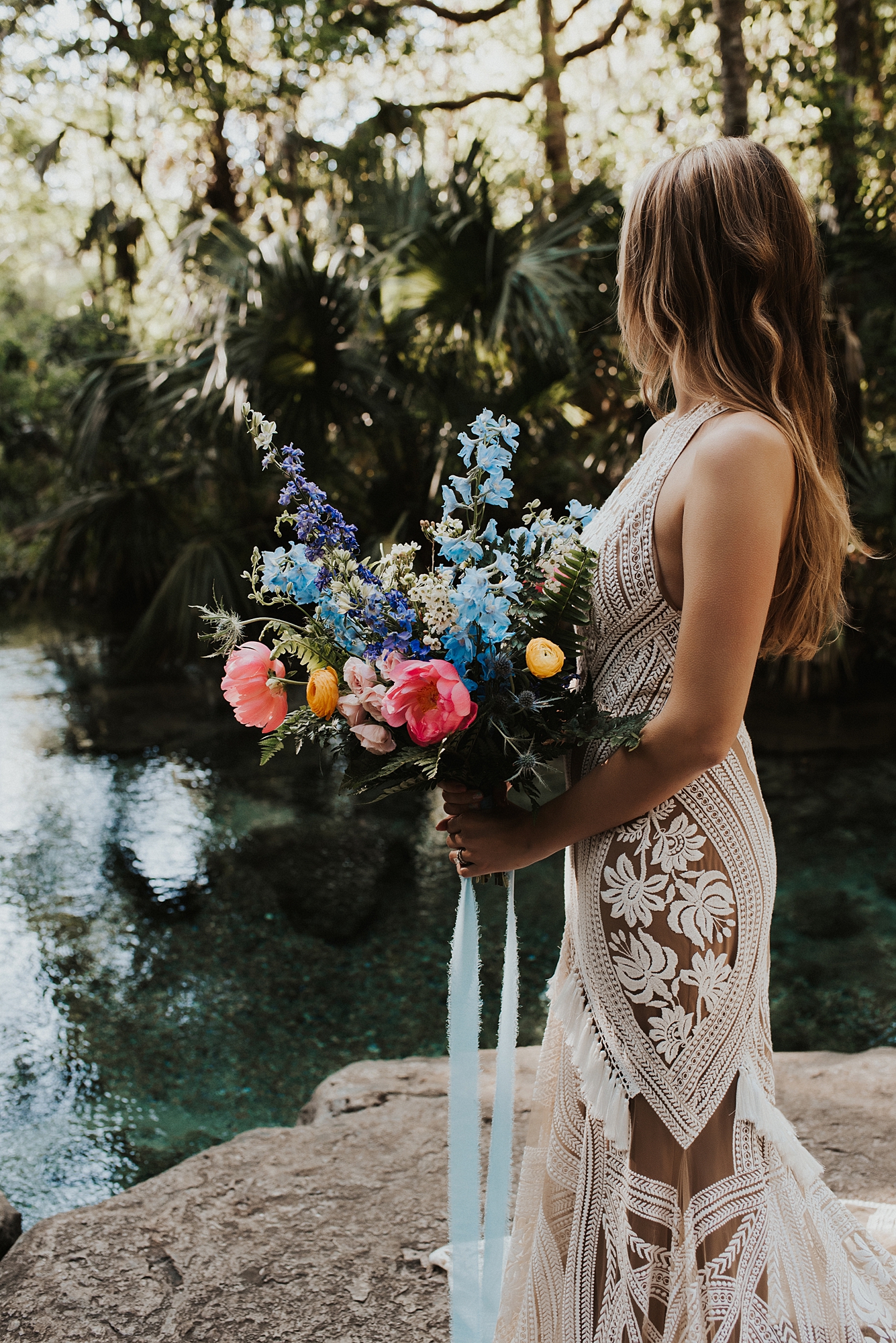Bride wearing Rue De Seine dress and holding a bright and colorful bouquet on rock platform at Kelly Park Rock Springs