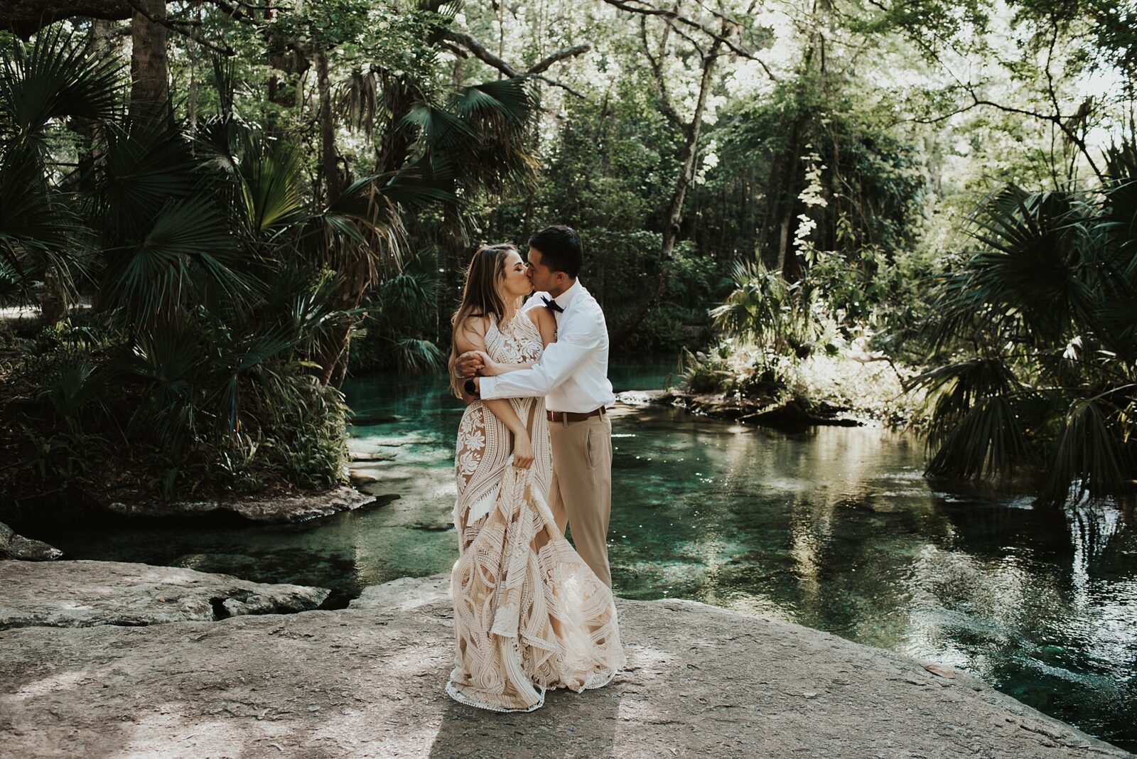 Groom holding bride in Rue De Seine dress and kissing her on the rock of Kelly Park Rock Springs