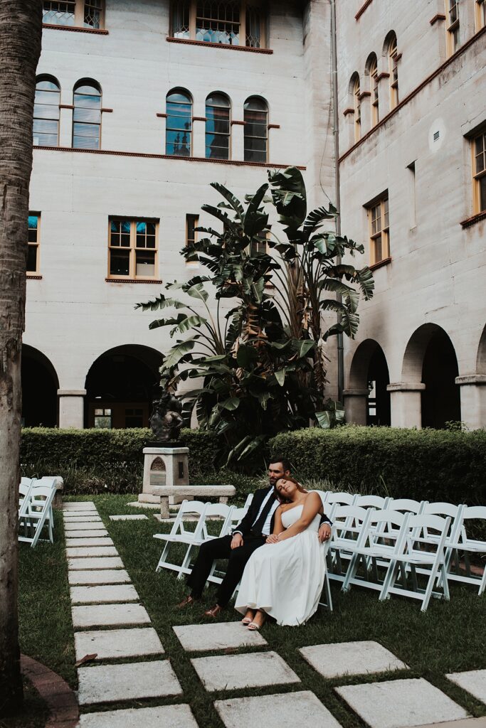 Bride and groom sitting on white ceremony chairs after their elopement at the Lightner museum courtyard