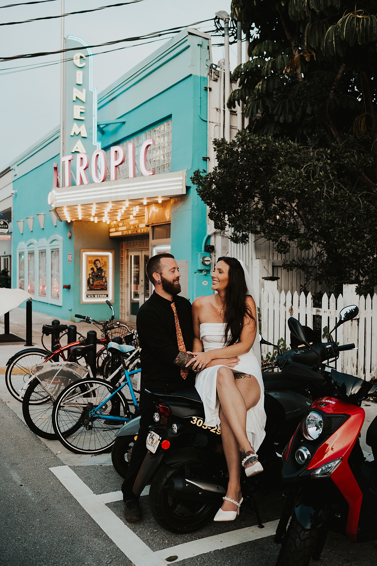Bride and groom leaning on mopeds in front of Tropic Cinema in key West after their elopement in September