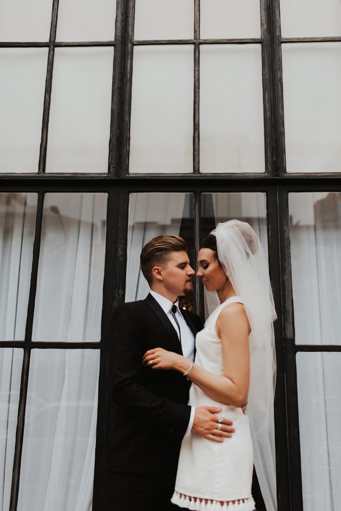 Bride and groom facing each other in front of black window