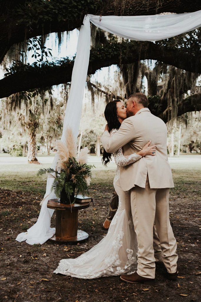 Bride and groom first kiss under oak trees in outdoor ceremony in Okeechobee Florida